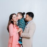 A man and a woman holding a baby in front of a white wall