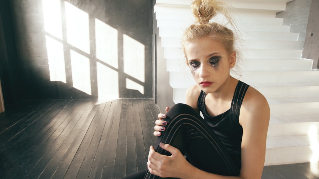 Sad young girl with smudged makeup sits on floor.
