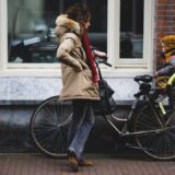woman in brown coat and blue denim jeans riding on black bicycle