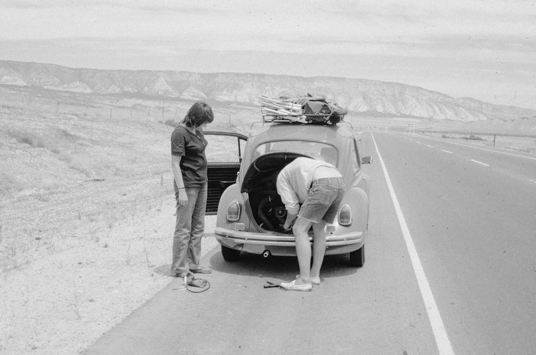 Two people working on a car on a roadside.