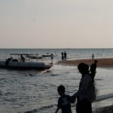 People on a beach with a boat in the water.