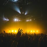 Publiek met opgestoken handen en lichtjes voor een verlicht concertpodium