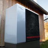 Buitenunit van een warmtepomp tegen een houten gevel