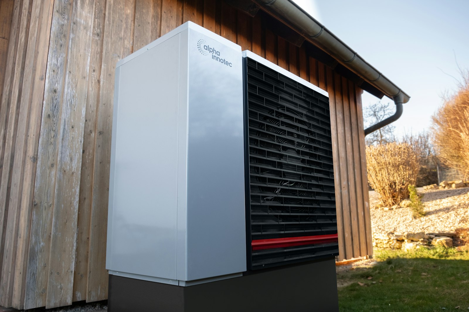 Buitenunit van een warmtepomp tegen een houten gevel