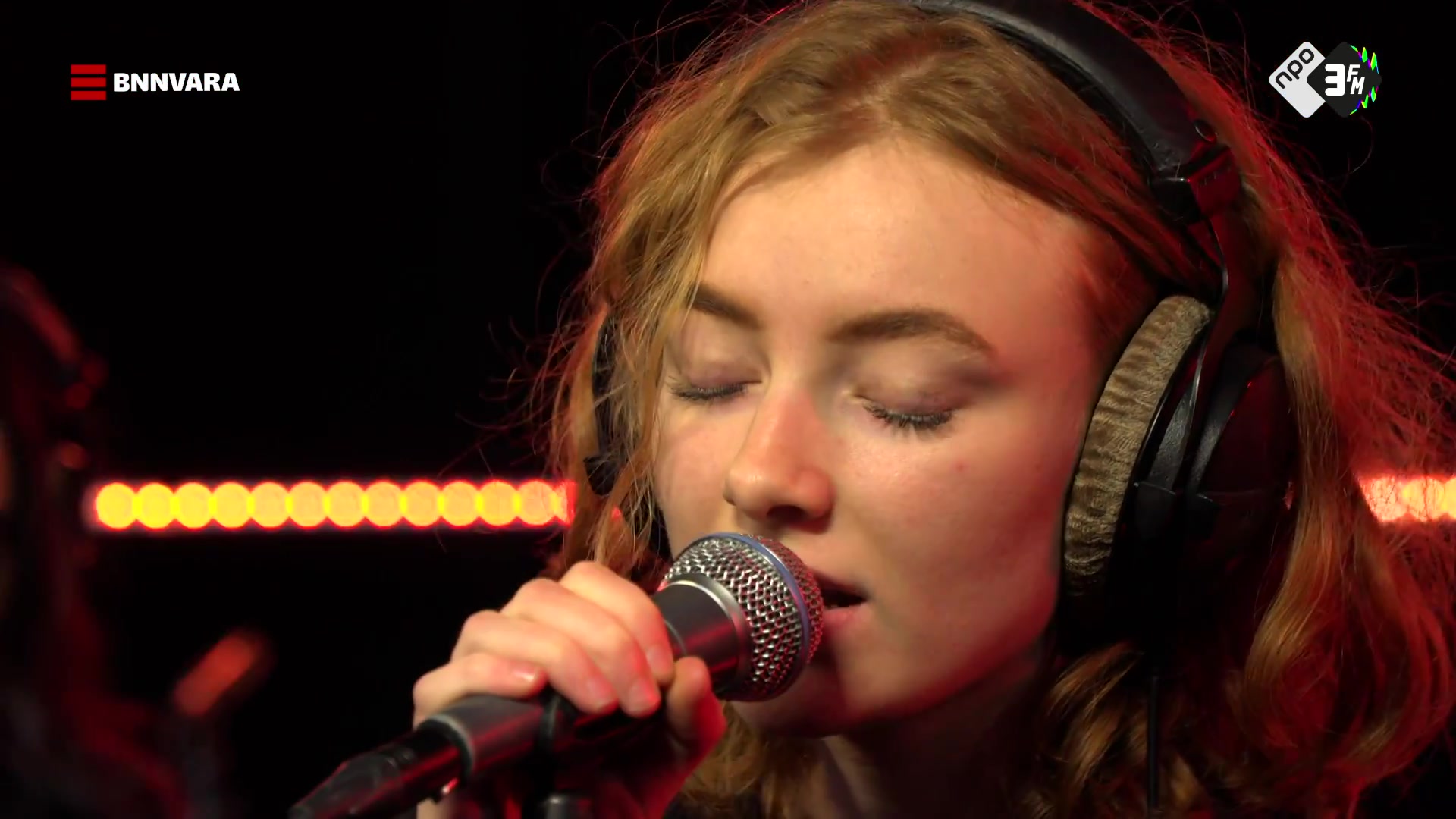 Zangeres Froukje zingt met een koptelefoon op achter de microfoon in een radiostudio