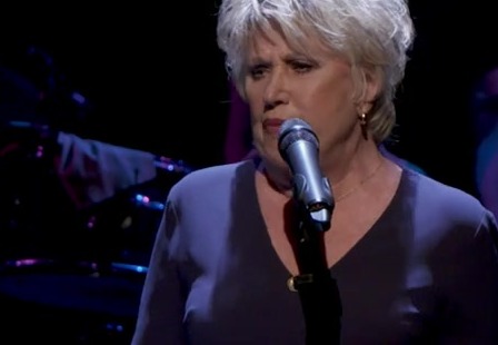 Jenny Arean zingt achter een microfoon op een donker podium
