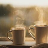 Twee koffiekopjes op een houten tafel bij een raam met avondlicht