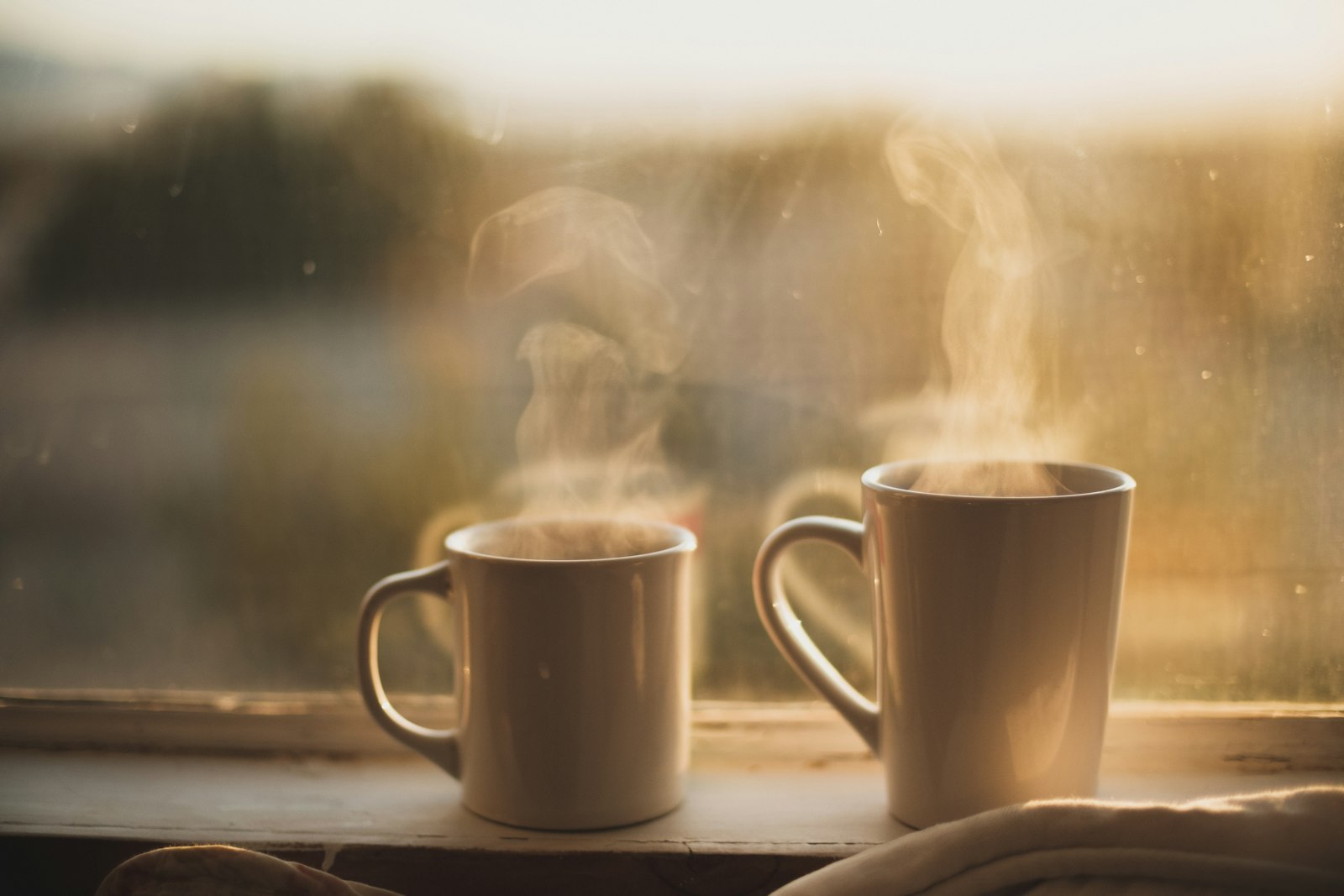 Twee koffiekopjes op een houten tafel bij een raam met avondlicht
