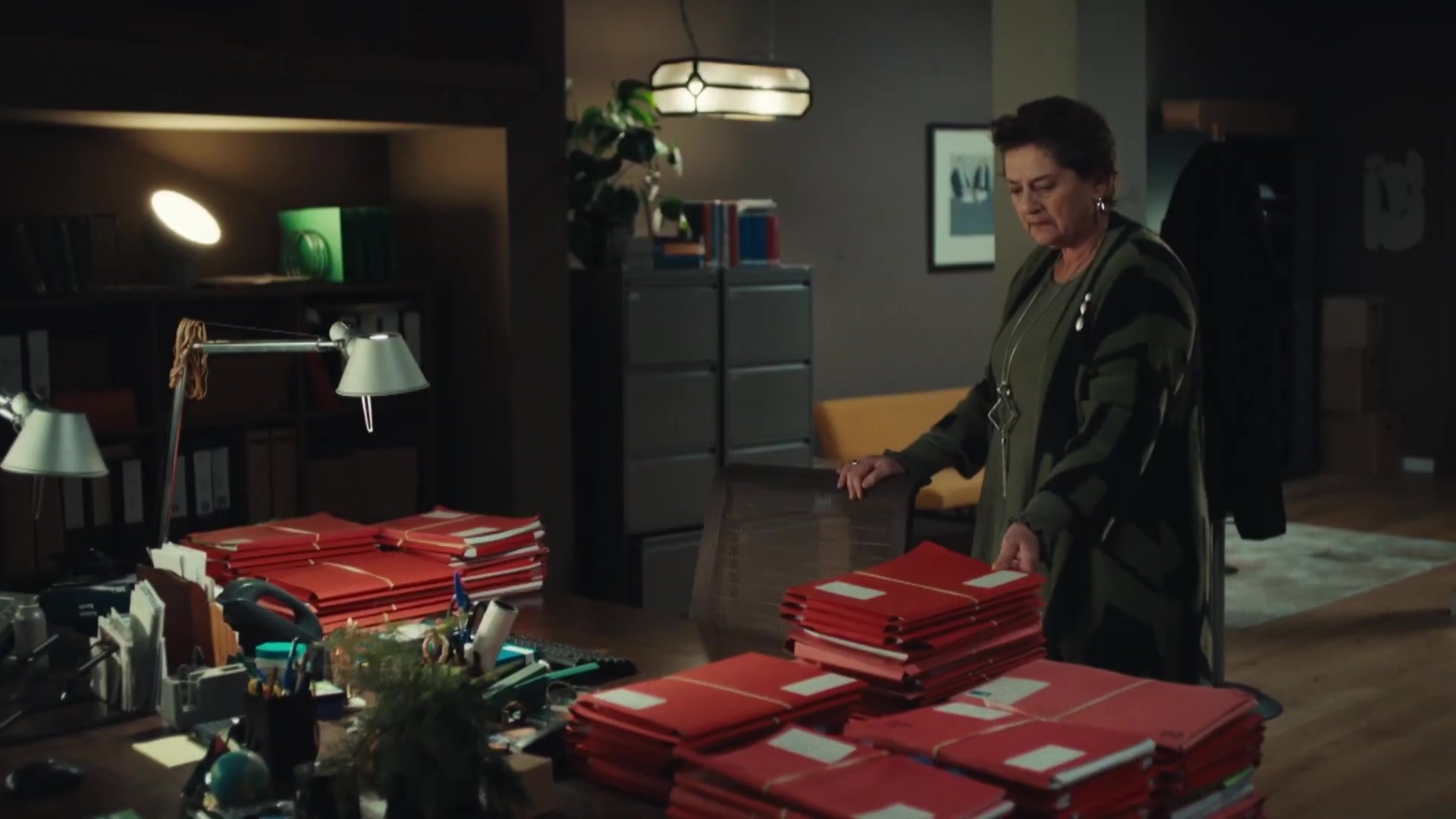 Een vrouw in een donker advocatenkantoor bij een tafel vol rode dossiermappen