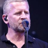 De zanger van Racoon zingt live op een podium met een oortje in