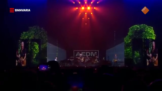 Acda en de Munnik op een podium met groene bomen en lichtshow tijdens een reünieconcert