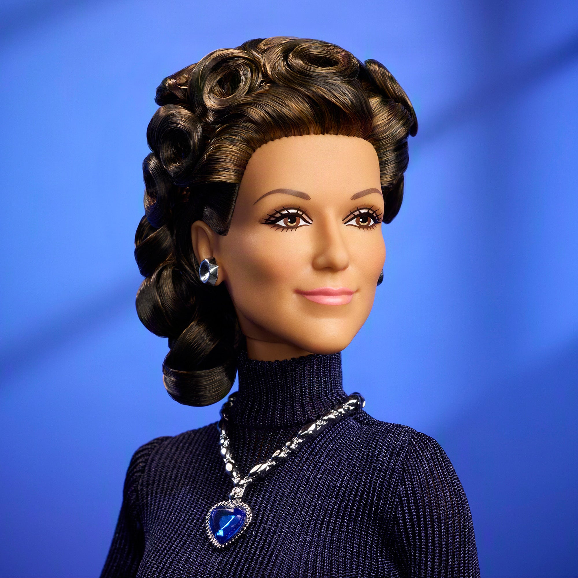 Close-up van de Céline Dion Barbie met donkere krullen, een donkerblauwe coltrui en een blauwe hartvormige ketting