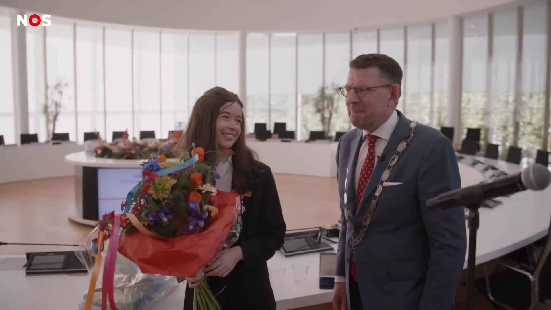 Jade Kops met een grote bos bloemen in een raadszaal