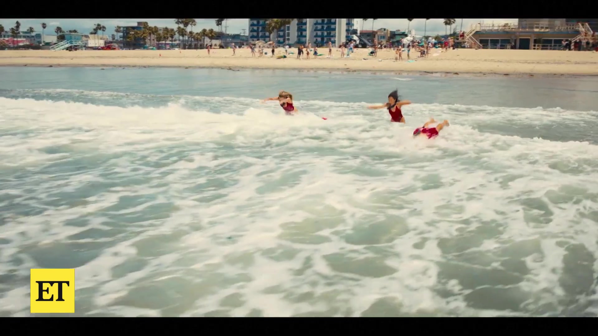 Drie strandwachten in rode badpakken rennen de branding in, uit de trailer van de nieuwe Baywatch