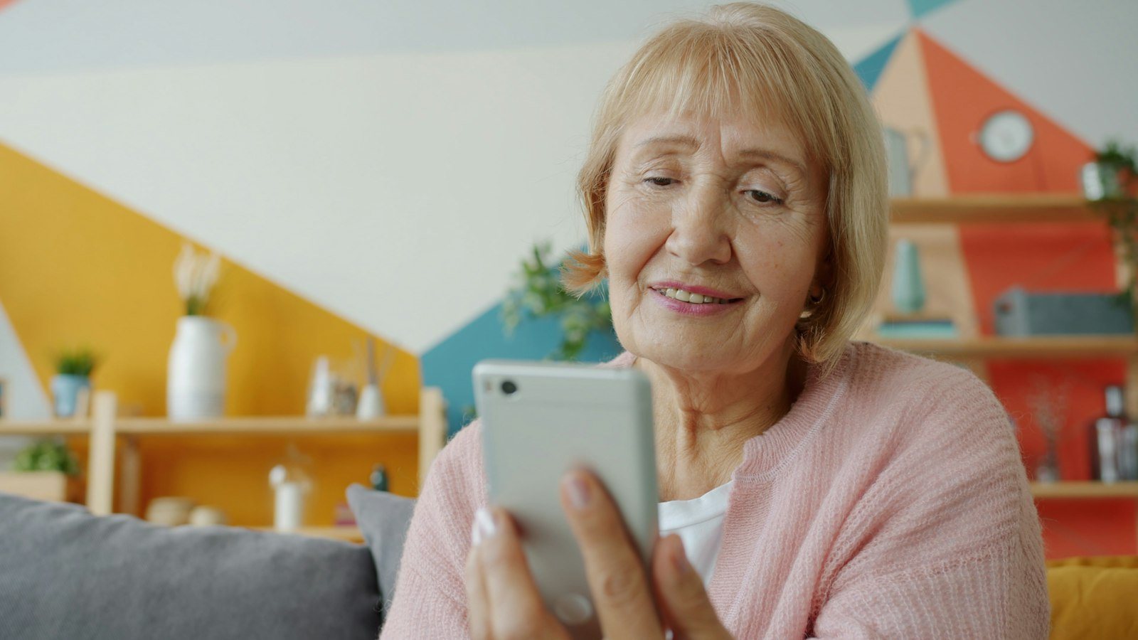 Oudere vrouw bekijkt lachend familiefoto's op haar smartphone