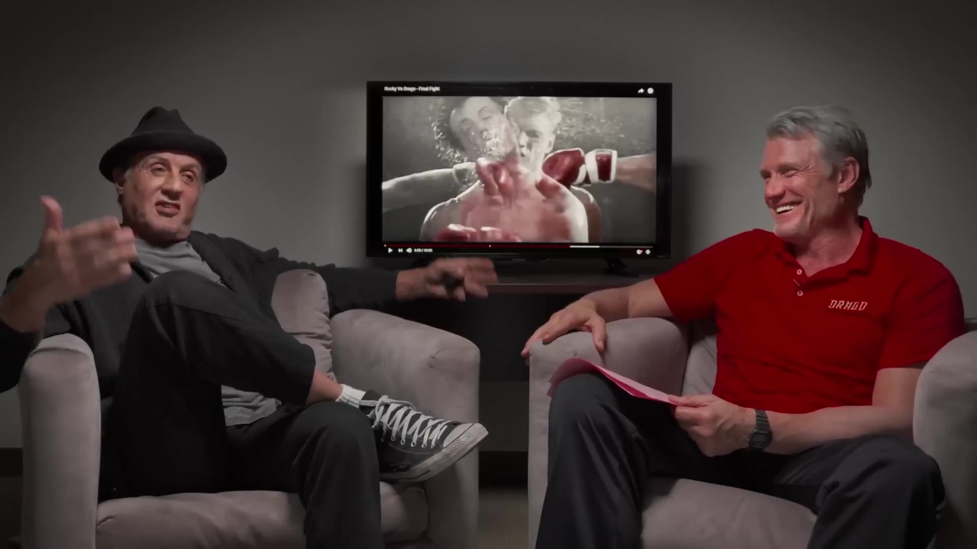 Sylvester Stallone en Dolph Lundgren in fauteuils terwijl ze terugkijken naar hun gevecht uit Rocky IV