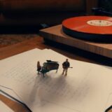 Suzan en Freek als miniatuurfiguren bij een vleugel naast een platenspeler, uit de clip van Pijnstiller