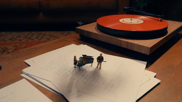 Suzan en Freek als miniatuurfiguren bij een vleugel naast een platenspeler, uit de clip van Pijnstiller