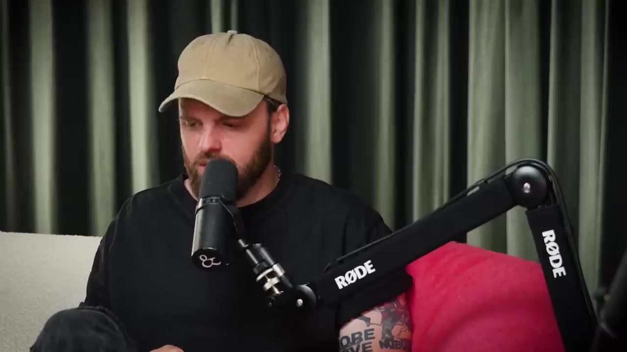 Tim Hofman met pet en baard aan tafel in een podcaststudio