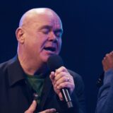 Paul de Leeuw zingt met gesloten ogen op het podium tijdens een concert van Paul & Vrienden