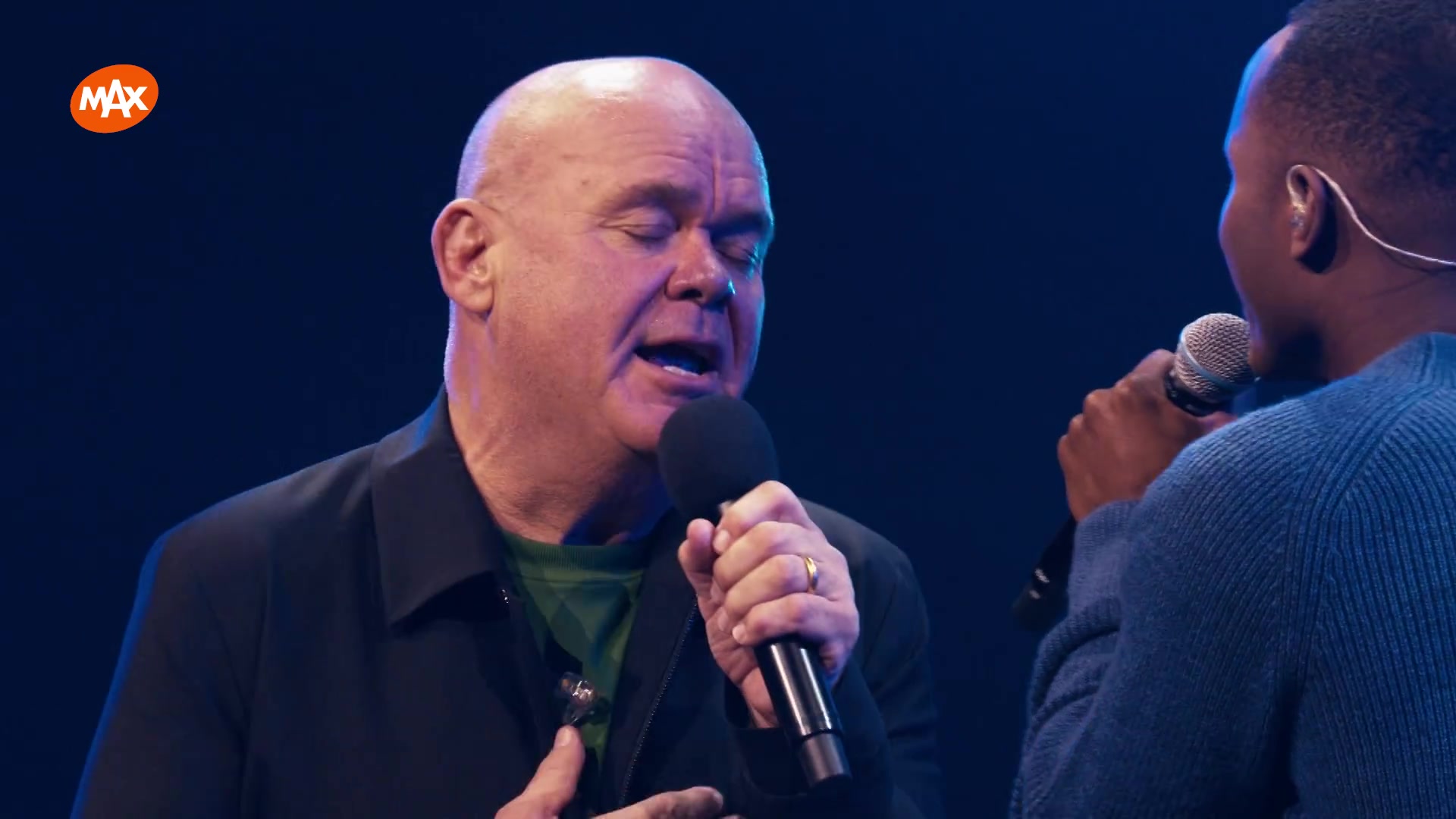 Paul de Leeuw zingt met gesloten ogen op het podium tijdens een concert van Paul & Vrienden